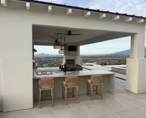 Modern white marble waterfall bar with woven wood stools overlooking a city valley.