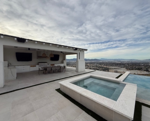 Modern square hot tub and infinity pool set into a light stone terrace with mountain views.