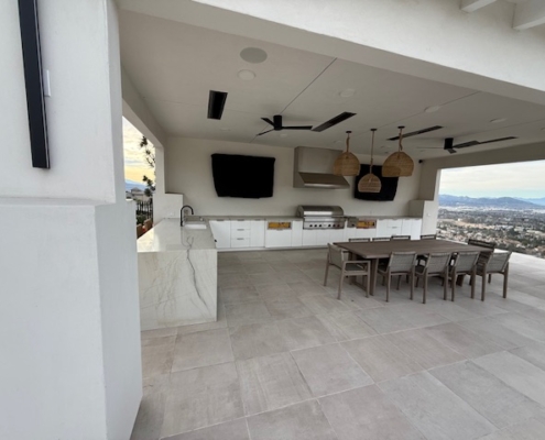 Modern white outdoor kitchen with stainless steel grill, hood, and dual flat-screen TVs.
